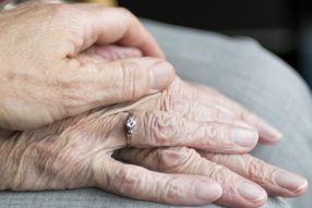 Eine jüngere Hand hält eine Hand von einer älteren Dame mit Ring.